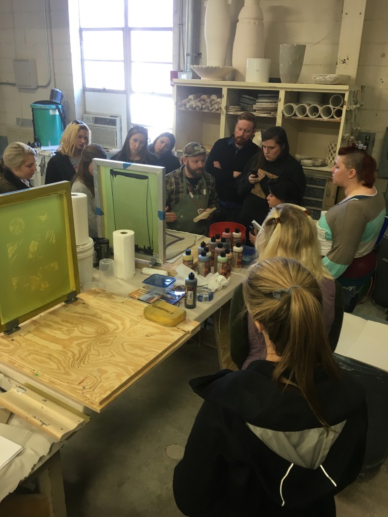 Workshop participants listen in as Israel Davis explains direct screen printing on clay slabs and newsprint transfer