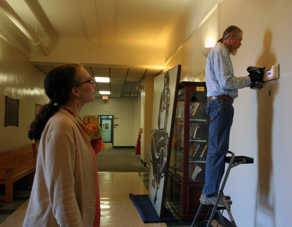 Emily Bibb and Bill Dooley measure the space and prepare to hang the larger than life size painting in the foyer of Morgan Hall.