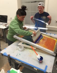 Checa Baldarelli screen printing with another student helping.