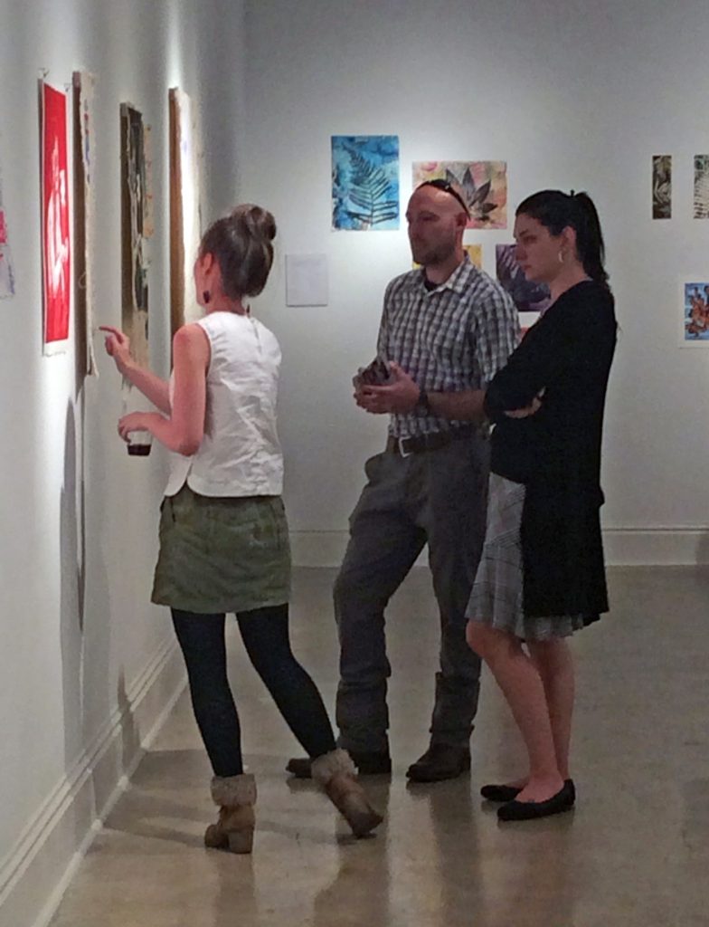A BFA major talks to visitors about her work on exhibit in the gallery.