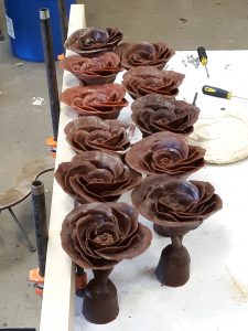 Two rows of wax camellias sit on a table in a workroom.