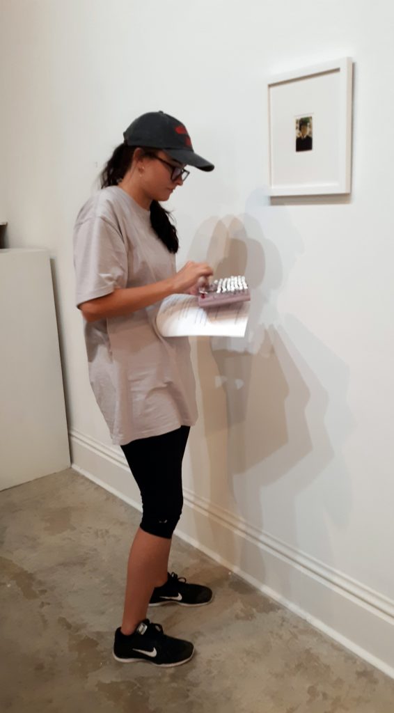 A student gallery worker attaches labels to the wall next to an artwork.