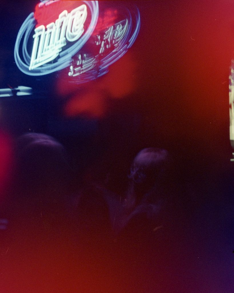 People sitting in a blurry, dark room lit by a neon "Lite" beer sign.