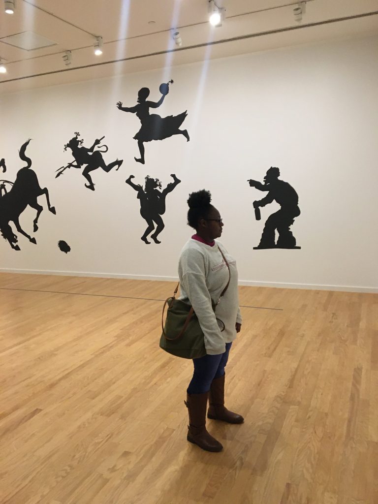 Graduate student stands in an exhibition hall before silhouettes.