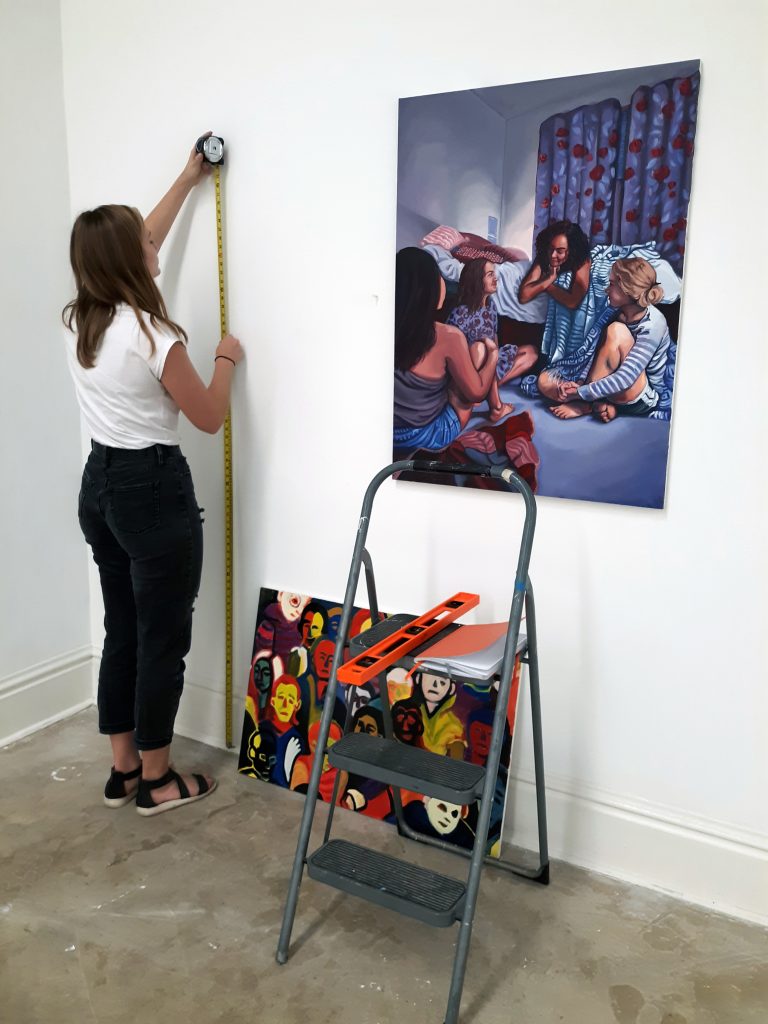 Student hanging artwork in a gallery.