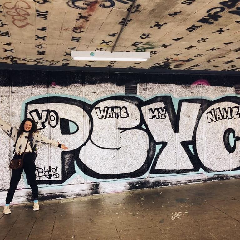 Girl posing next to graffiti art painted on wall.