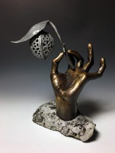 bronze sculpture of a hand holding a stem with leaf and nut