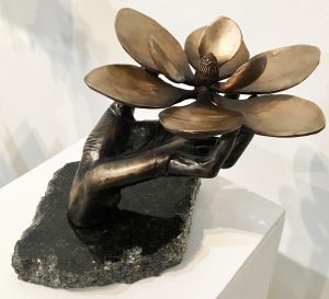 bronze sculpture of an outstretched hand holding out a magnolia blossom.