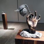 bronze sculpture of a hand holding a twig with nut and leaf