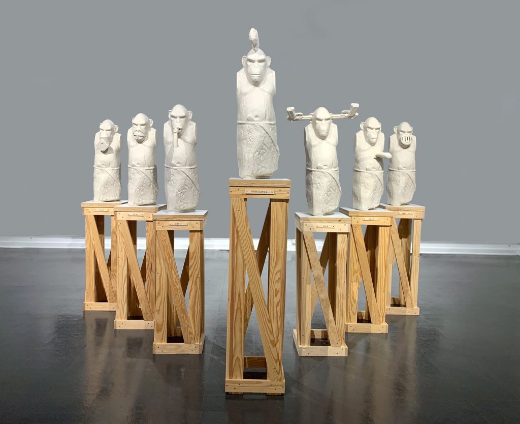 sculpture of seven apes in v-formation, on wood pedestals
