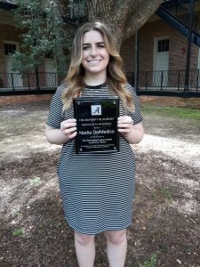 Student holding an award plaque, underneath a tree.