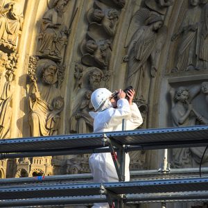 Person in hazmat suit taking photos on scaffolding outside a cathedral entrance.