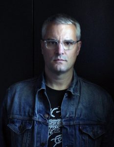 head and shoulders of a white male, mid-to-late 30s, in a denim jacket, mostly in shadow